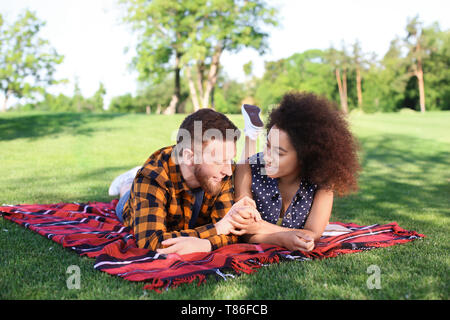 Young loving interracial couple resting in park on spring day Stock Photo