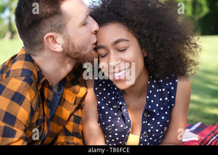 Young loving interracial couple resting in park on spring day Stock Photo