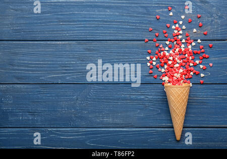 Cone with scattered heart-shaped candies on wooden background