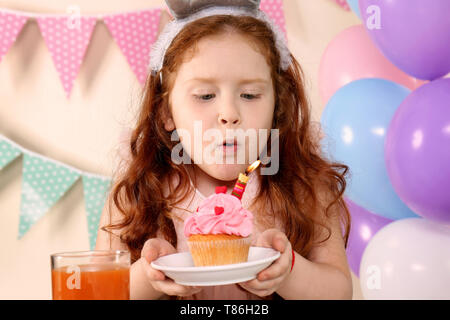 Little girl blowing out candle on birthday cupcake at home Stock Photo