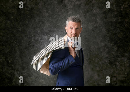 Handsome mature man in suit with shopping bags on dark textured background Stock Photo