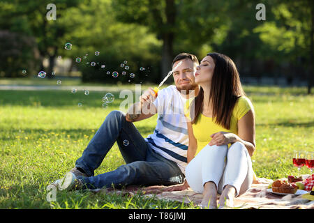 Happy couple blowing soap bubbles in park on spring day Stock Photo