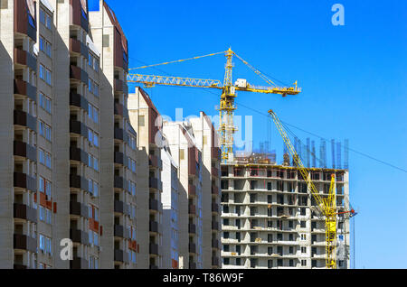 Finished Apartment Building and a New High-Rise Building Construction Site with Yellow Cranes against Blue Sky. Real Estate, Residential Buildings Urb Stock Photo