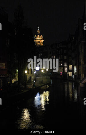 Reflections of street lights on canal. Illuminated Basilica of Saint Nicholas on the background. Amsterdam, Netherlands. Stock Photo