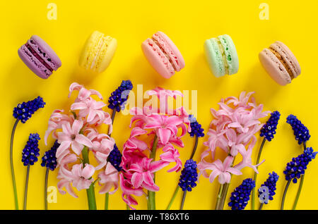 Blue muscari flowers, pink hyacinth and macarons or macaroons on yellow background. Overhead shot. Flat lay. Celebration concept. Stock Photo