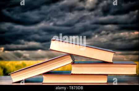 books stacked on top of each other against dark clouds Stock Photo