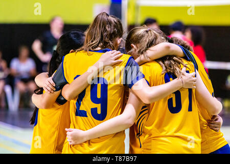 Female volleyball players in yellow uniform huddling together before starting the game Stock Photo