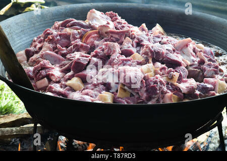 Small sliced meat cooked on a a very big pan using fire wood: Raw meat Stock Photo