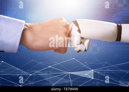 Robot And Human Hand Making Fist Bump On Blue Digital Backdrop Stock Photo
