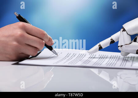 Robotic Hand Assisting Person For Filling Form Over Reflective Desk Stock Photo