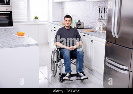 Smiling Young Handicapped Man Sitting On Wheelchair In Kitchen Stock Photo
