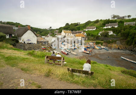 People sat watching traditional fishing boats on the beach of the small fishing village of Cadgwith,Cornwall, England,UK. Stock Photo