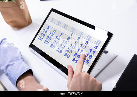 Close-up Of A Businessman's Hand Using Calendar On Laptop Over Desk Stock Photo