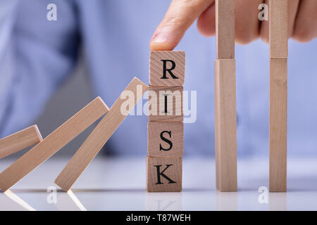 Businessperson's Finger Over Risk Wooden Blocks Stopping Dominos From Falling On Reflective Desk Stock Photo