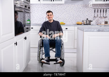 Smiling Young Handicapped Man Sitting On Wheelchair In Kitchen Stock Photo