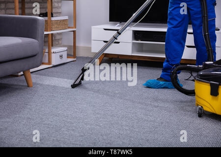 Low Section Of A Male Janitor Cleaning Carpet With Vacuum Cleaning In The Living Room Stock Photo