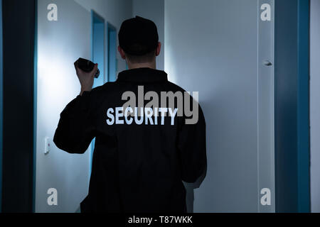 Rear View Of Male Security Guard With Flashlight Standing In Corridor Of The Building Stock Photo