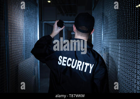 Rear View Of A Security Guard Standing In The Warehouse Holding Flashlight Stock Photo