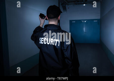 Rear View Of A Male Security Guard With Flashlight Standing In Corridor Stock Photo