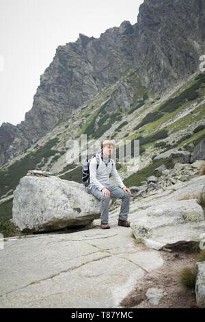 tourist with backpack sitting on boulder in mountains Stock Photo