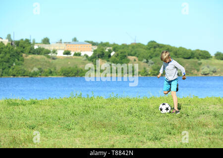 Cute boy playing football near river Stock Photo