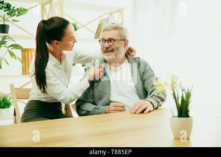 A daughter or granddaughter spends time with the grandfather or senior man. Family or fathers' day, positive emotions and happieness. Lifestyle portrait at home. Girl taking care about dad. Stock Photo