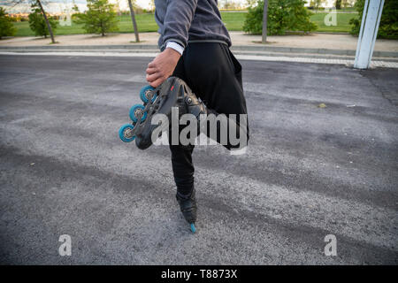 Crop back view of young cool man in sportswear holding roller skate with hand on road in park Stock Photo