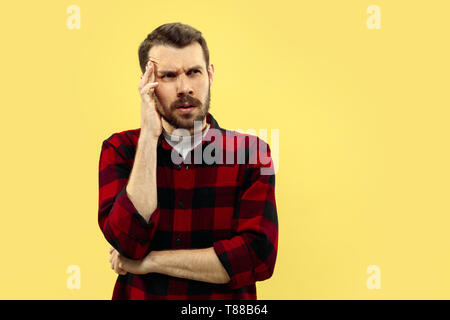 Half-length close up portrait of young man in shirt on yellow background. The human emotions, facial expression concept. Front view. Trendy colors. Negative space. Seriously thinking . Stock Photo
