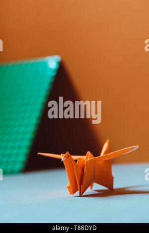 Orange origami bird, a bird made of paper-origami. (Soft focus), on light colored fabric cushion Stock Photo