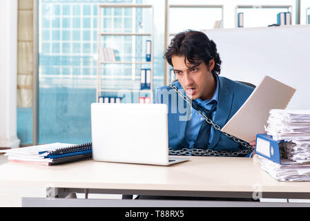 Chained male employee unhappy with excessive work Stock Photo