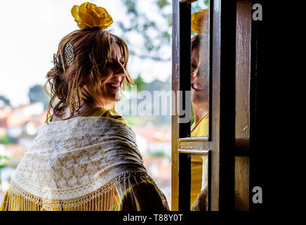 A Spanish woman wearing a bright yellow traditional flamenco style dress in Andalusia standing in front of a door and reflecting the face in the glass Stock Photo