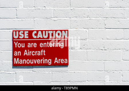 Aircraft manouvering red and white cautionary warning sign hung on painted brick wall. Stock Photo