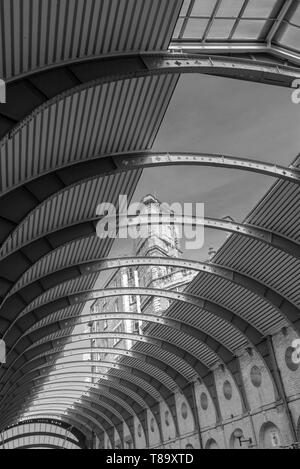 The curving canopy at York Railway Station with a view through to a towering building and the sky.  In black and white. Stock Photo