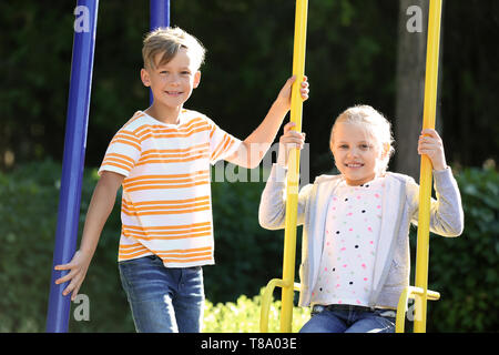 Cute boy pushing little girl on swings outdoors Stock Photo