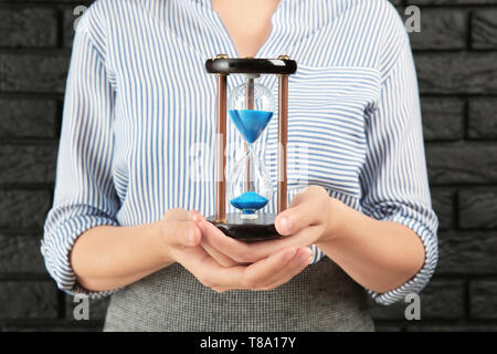 Woman with hourglass against brick wall, closeup. Time management concept Stock Photo