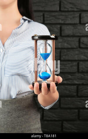 Woman with hourglass against brick wall. Time management concept Stock Photo