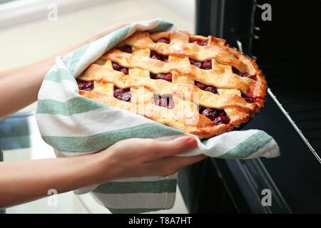 Woman taking baking pan with delicious pie from electric oven in