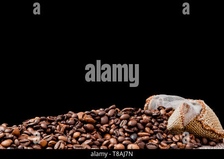 Fresh roasted coffee beans falling out the sack on the black background. Brown coffee beans scattered from bag on the table Stock Photo