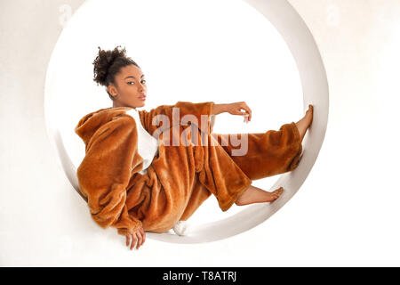 Young woman in bunny kigurumi sitting in hole isolated on white background looking camera curious Stock Photo