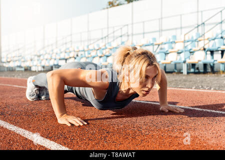 Sporty Lifestyle. Young woman on stadium doing push ups looking forward motivated Stock Photo