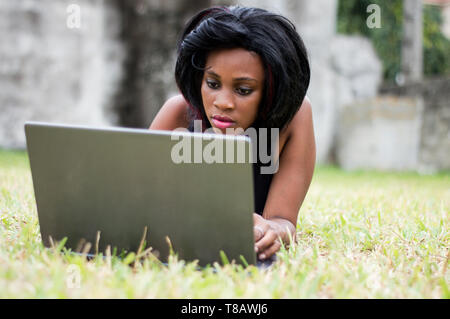 pretty woman lying on herbs, is focused on her laptop in front of her. Stock Photo