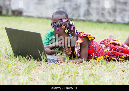 two children lying in the garden use a laptop Stock Photo