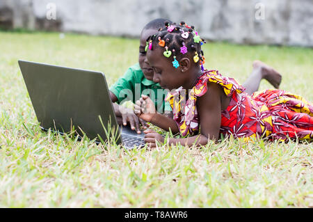 Happy children using a laptop lying in the garden Stock Photo