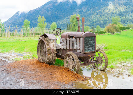 Vintage tractor farm equipment on a real farm, rusted and broken down, parked in mud, but a historical remnant on display. Stock Photo