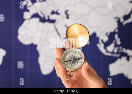 Woman holding vintage compass against blurred world map, closeup Stock Photo