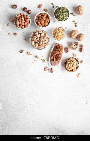 Various Nuts in  bowls on white background, top view, copy space. Nuts assortment frame - pecans, hazelnuts, walnuts, pistachios, almonds, pine nuts,  Stock Photo