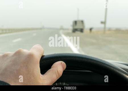 View of driver's hands on the wheel of a car that travels on the highway near parked on the side of the truck Stock Photo