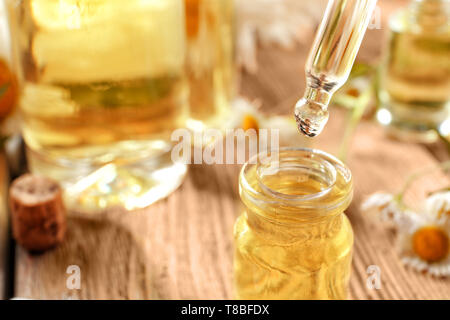 Chamomile essential oil dripping from pipette into bottle, closeup Stock Photo