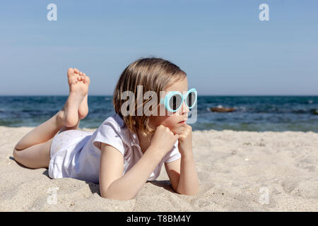 Funny little girl (7 years old) in sunglasses lies on the beach. Selective focus.