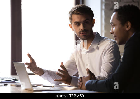 Diverse office workers sitting at workplace discussing working moments Stock Photo